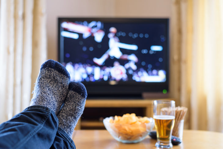 Television, TV watching (basketball game) with feet on table eating snacks and drinking beer - stock photo - Image